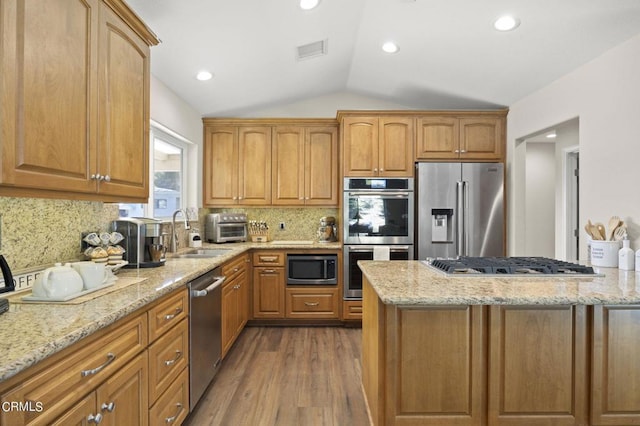 kitchen with sink, backsplash, lofted ceiling, appliances with stainless steel finishes, and hardwood / wood-style flooring