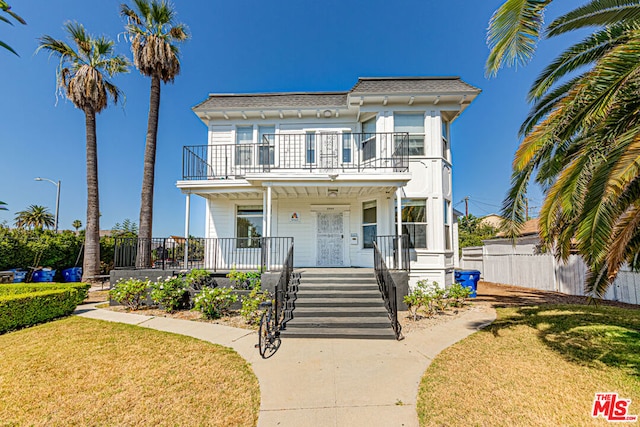 view of front of house with a front yard, a balcony, and covered porch