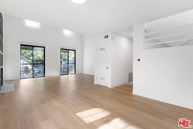 unfurnished living room featuring a towering ceiling and light hardwood / wood-style floors