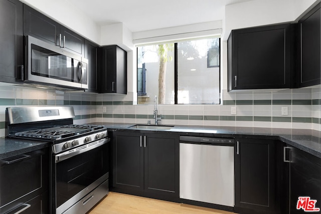 kitchen featuring light hardwood / wood-style floors, dark stone counters, sink, stainless steel appliances, and backsplash