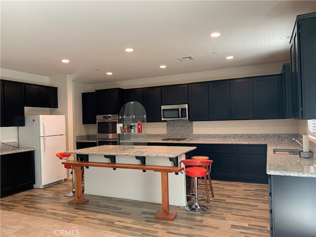 kitchen with appliances with stainless steel finishes, a kitchen island, sink, and light hardwood / wood-style flooring