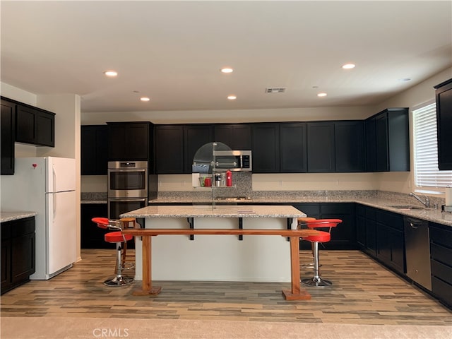 kitchen with light wood-type flooring, light stone countertops, stainless steel appliances, sink, and a breakfast bar area