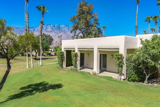 rear view of house with a lawn, a mountain view, and a patio area