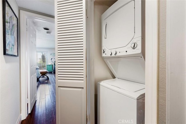 clothes washing area with stacked washing maching and dryer and dark wood-type flooring