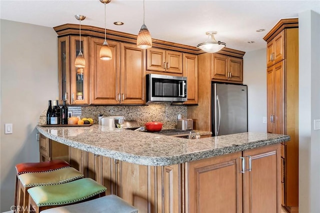 kitchen with tasteful backsplash, kitchen peninsula, hanging light fixtures, appliances with stainless steel finishes, and a kitchen breakfast bar