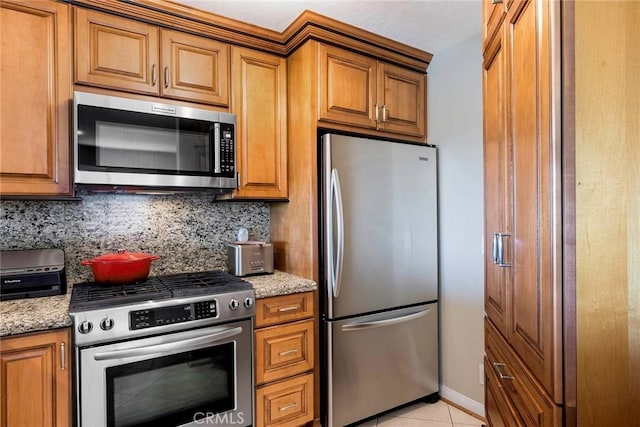 kitchen with light tile patterned floors, backsplash, light stone counters, and stainless steel appliances