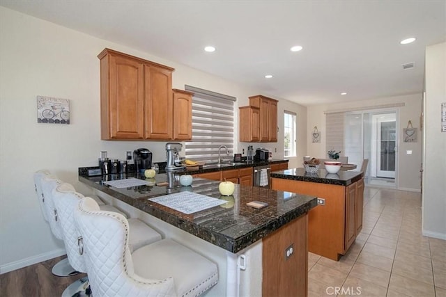 kitchen featuring kitchen peninsula, a kitchen bar, stainless steel dishwasher, light tile patterned floors, and a kitchen island