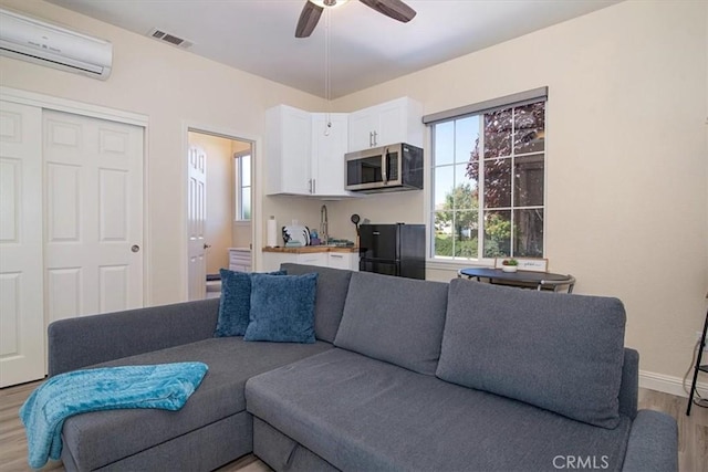 living room with a wall mounted AC, ceiling fan, and light wood-type flooring