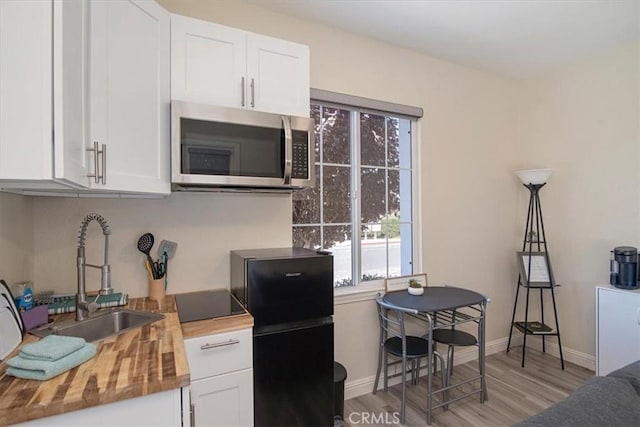 kitchen featuring wood counters, light wood-type flooring, white cabinetry, and black refrigerator