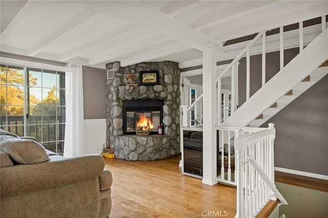 living room featuring a stone fireplace, hardwood / wood-style floors, and beamed ceiling