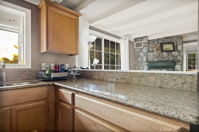 kitchen with beamed ceiling, sink, light stone countertops, and a fireplace