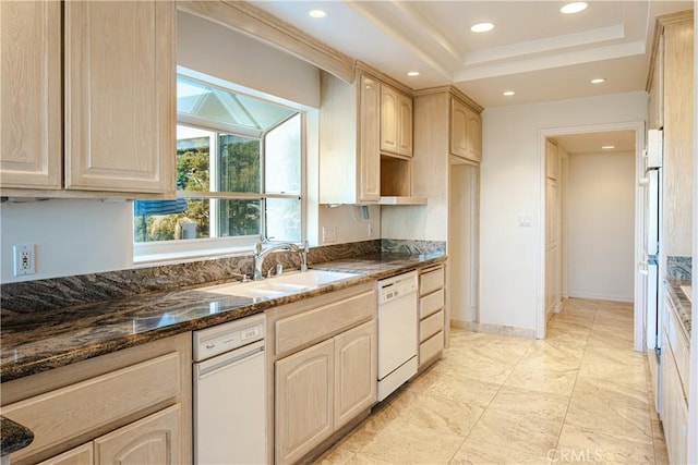 kitchen with dishwasher, sink, dark stone countertops, light brown cabinets, and a tray ceiling