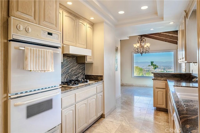 kitchen with pendant lighting, white appliances, light brown cabinetry, backsplash, and lofted ceiling with beams