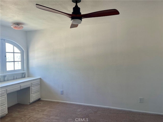 unfurnished office featuring light carpet, built in desk, and ceiling fan