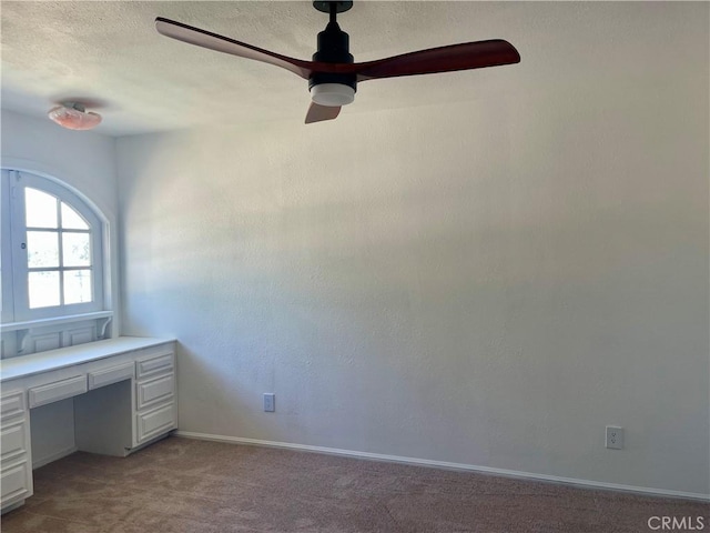 unfurnished office featuring light carpet, built in desk, and a textured ceiling