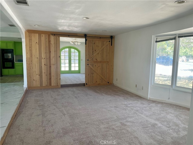 carpeted empty room with a wealth of natural light, a textured ceiling, and a barn door