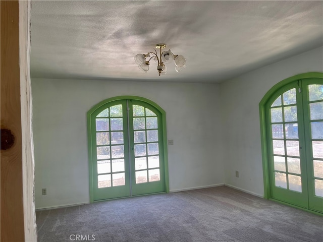 carpeted empty room featuring a healthy amount of sunlight, a textured ceiling, and french doors