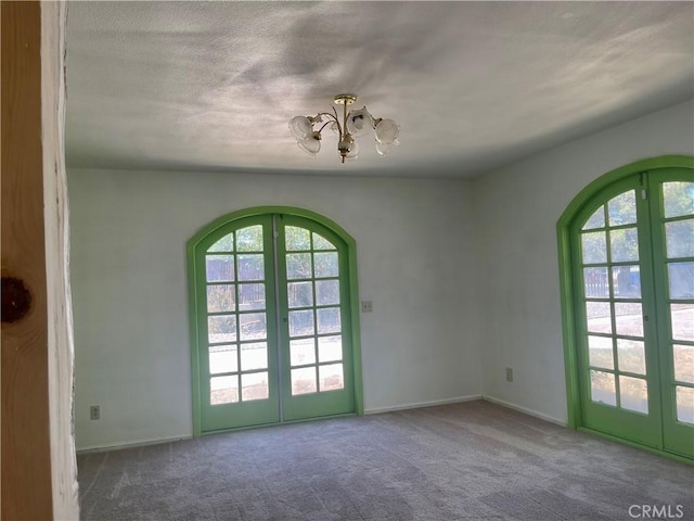 spare room featuring a textured ceiling, french doors, carpet flooring, and an inviting chandelier