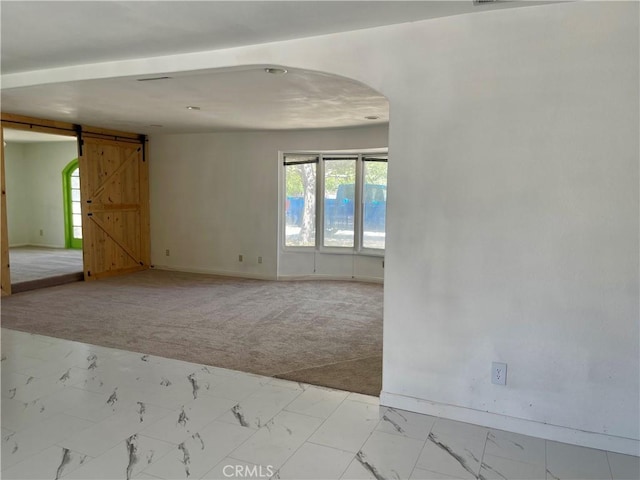 unfurnished room featuring a barn door and light carpet