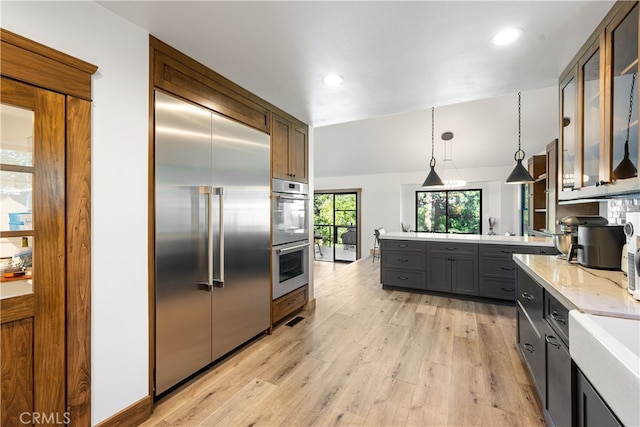 kitchen with appliances with stainless steel finishes, light stone countertops, hanging light fixtures, and light hardwood / wood-style flooring