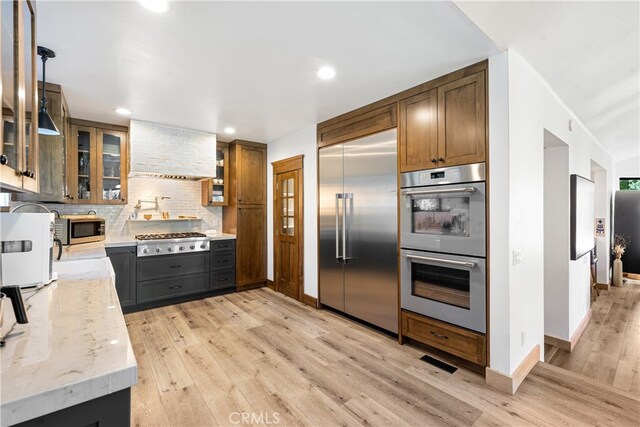 kitchen featuring stainless steel appliances, pendant lighting, light stone counters, and light wood-type flooring