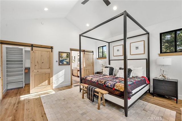 bedroom with ceiling fan, light hardwood / wood-style floors, a barn door, and lofted ceiling