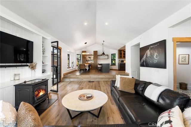 living room featuring built in shelves, vaulted ceiling, light wood-type flooring, and a wood stove