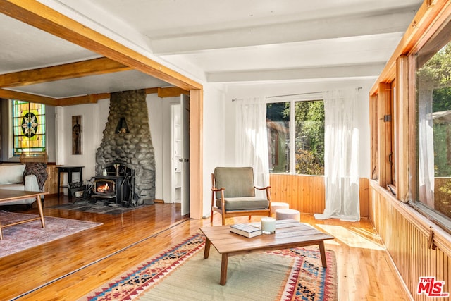 sitting room featuring beamed ceiling, hardwood / wood-style flooring, and a wood stove