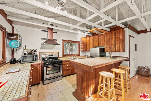 kitchen with wall chimney exhaust hood, sink, tile countertops, appliances with stainless steel finishes, and kitchen peninsula