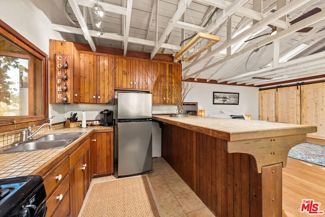 kitchen with black stove, sink, light tile patterned floors, stainless steel fridge, and beamed ceiling