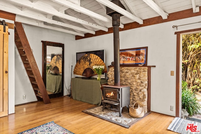 living area featuring wood ceiling, hardwood / wood-style floors, a barn door, beamed ceiling, and a wood stove