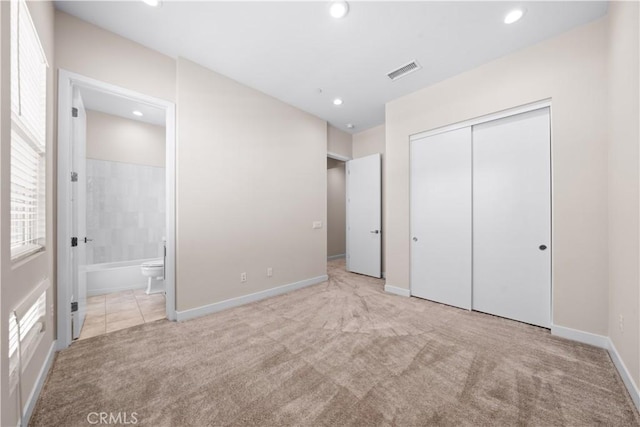 unfurnished bedroom featuring light colored carpet, ensuite bath, and a closet