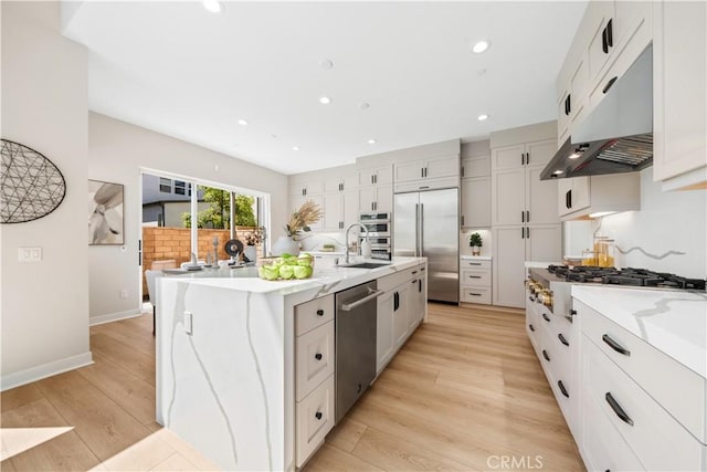 kitchen with white cabinetry, sink, light hardwood / wood-style floors, a center island with sink, and appliances with stainless steel finishes