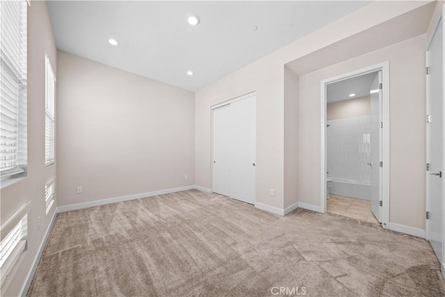 unfurnished bedroom featuring light carpet, a closet, and ensuite bathroom