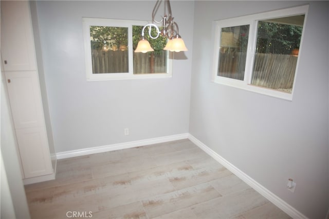 unfurnished dining area featuring an inviting chandelier and light hardwood / wood-style floors