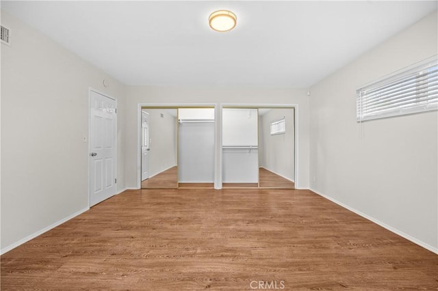 unfurnished bedroom with two closets, baseboards, light wood-style floors, and visible vents