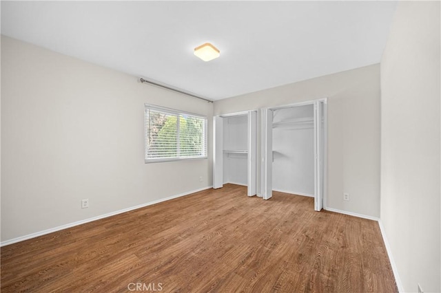 unfurnished bedroom featuring baseboards, wood finished floors, and multiple closets