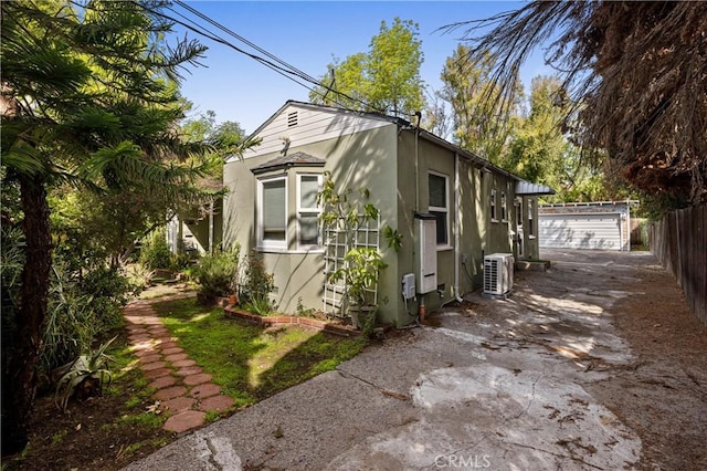 view of side of property with fence, stucco siding, driveway, an outdoor structure, and a detached garage