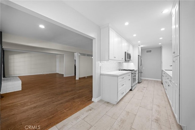kitchen featuring tasteful backsplash, white cabinetry, light wood-style floors, light countertops, and appliances with stainless steel finishes