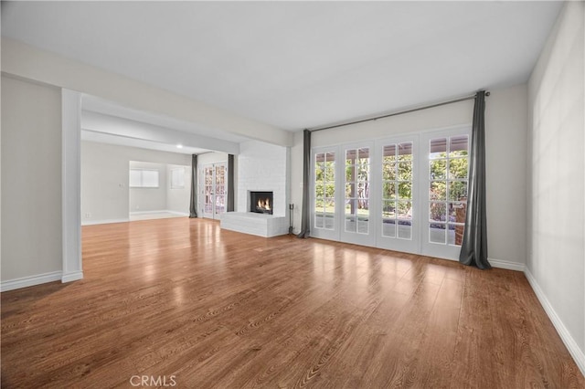 unfurnished living room featuring wood finished floors, a brick fireplace, and baseboards