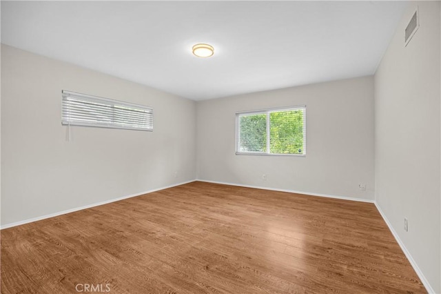 spare room with baseboards, wood finished floors, and visible vents