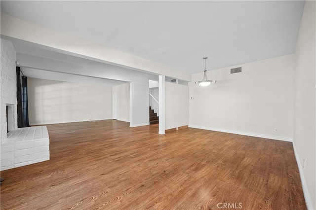 unfurnished living room with stairway, wood finished floors, a fireplace, baseboards, and visible vents
