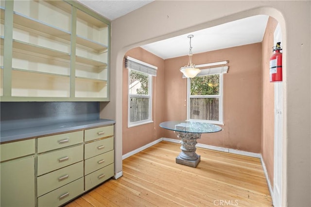 unfurnished dining area featuring arched walkways, light wood finished floors, and baseboards