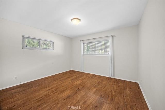 empty room with a wealth of natural light, wood finished floors, and baseboards