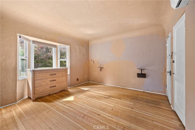 spare room with a wall mounted air conditioner, baseboards, and light wood-style floors