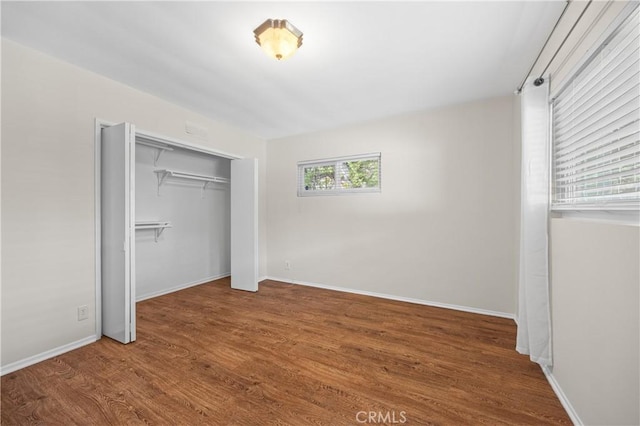 unfurnished bedroom featuring baseboards, wood finished floors, and a closet