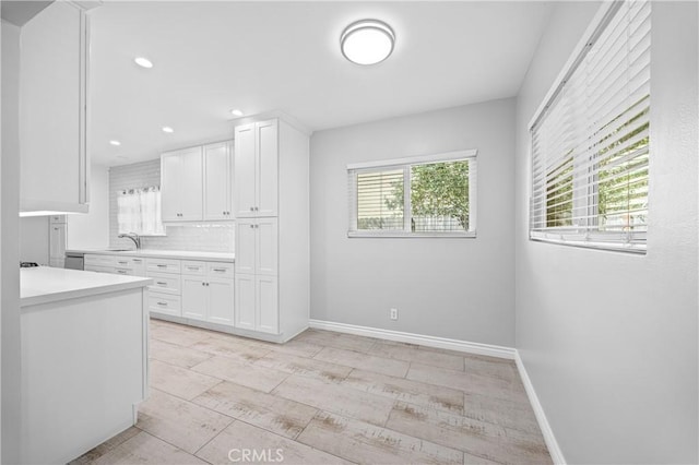 kitchen with white cabinets, light countertops, a sink, and tasteful backsplash