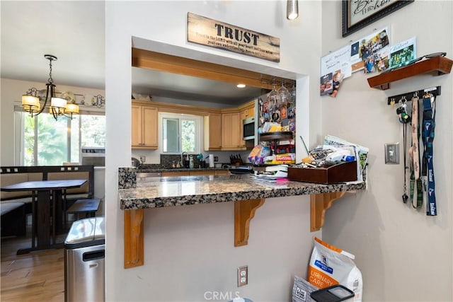 kitchen featuring light hardwood / wood-style floors, kitchen peninsula, a breakfast bar area, hanging light fixtures, and a chandelier