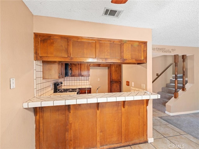 kitchen featuring light tile patterned floors, stove, a textured ceiling, decorative backsplash, and kitchen peninsula