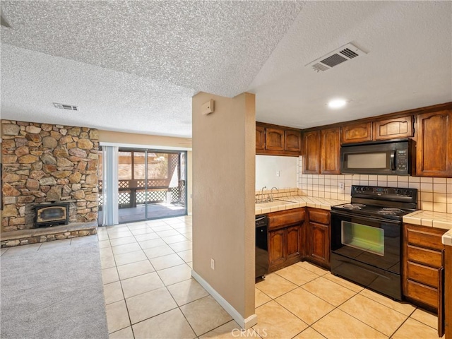 kitchen with light tile patterned flooring, sink, tile countertops, black appliances, and backsplash